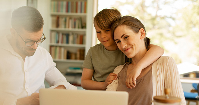 Familie ved spisebord med laptop, sol kommer inn utenfra.
