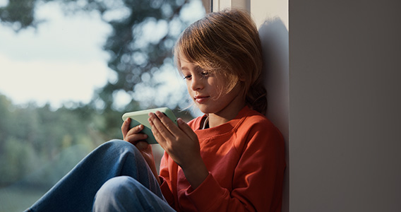 Barn slapper av med mobilen i vinduskarmen