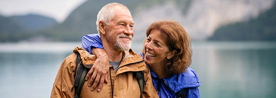Smilende, eldre par holder rundt hverandre, ute på tur i naturen.