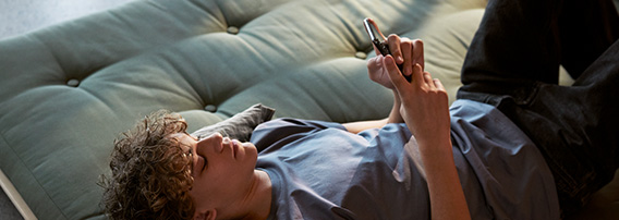 Ung mann ligger på ryggen på en grønn divan og ser på mobiltelefonen